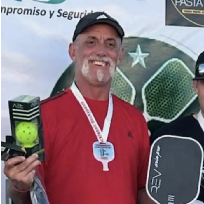 Scottsdale pickleball coach, Curtis Aylward holding up pickleball balls and a paddle with a winning medal around his neck.